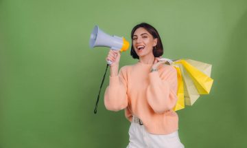 young-woman-in-casual-peach-sweater-isolated-on-green-olive-color-wall-shout-in-megaphone-holding-shopping-bags-announces-discounts-sale-promotion (1)